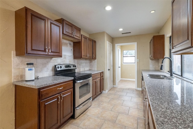 kitchen featuring tasteful backsplash, sink, light tile patterned floors, dark stone countertops, and stainless steel electric range