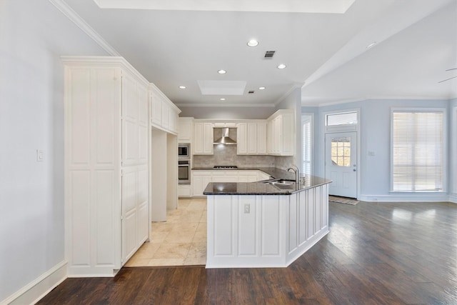 kitchen with appliances with stainless steel finishes, kitchen peninsula, wall chimney exhaust hood, white cabinets, and sink