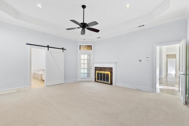 unfurnished living room featuring a fireplace, ceiling fan, a barn door, a tray ceiling, and light colored carpet