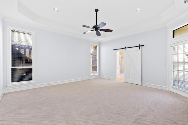 carpeted spare room with a wealth of natural light, ceiling fan, a barn door, a tray ceiling, and ornamental molding