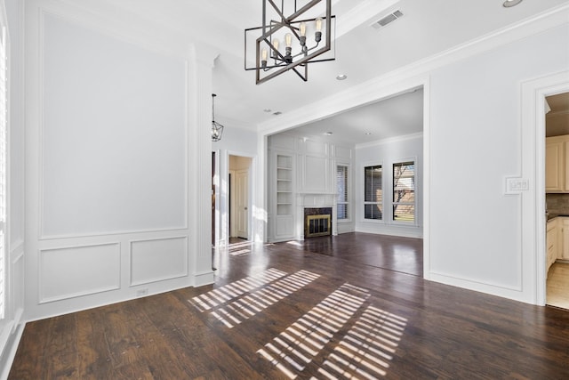 unfurnished living room with crown molding, built in shelves, hardwood / wood-style floors, a fireplace, and an inviting chandelier