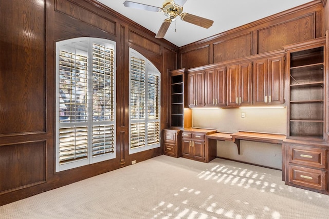 unfurnished office featuring built in desk, ceiling fan, wooden walls, and light carpet