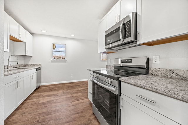 kitchen with light stone countertops, sink, stainless steel appliances, white cabinets, and hardwood / wood-style flooring