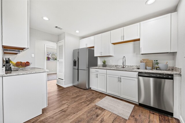 kitchen with hardwood / wood-style flooring, white cabinetry, sink, stainless steel appliances, and light stone counters