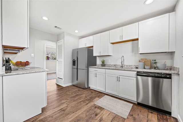 kitchen with appliances with stainless steel finishes, sink, light stone counters, dark hardwood / wood-style flooring, and white cabinets