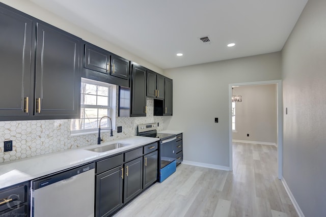 kitchen featuring light stone countertops, decorative backsplash, stainless steel appliances, sink, and light hardwood / wood-style flooring