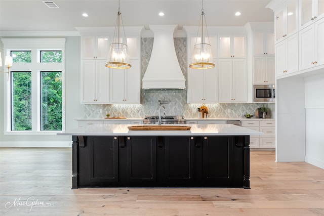 kitchen featuring stainless steel microwave, a center island with sink, light countertops, and custom range hood