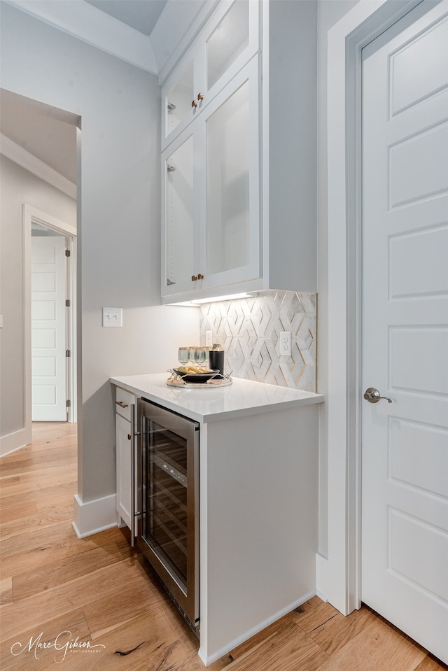 bar featuring wine cooler, white cabinetry, light hardwood / wood-style floors, and decorative backsplash