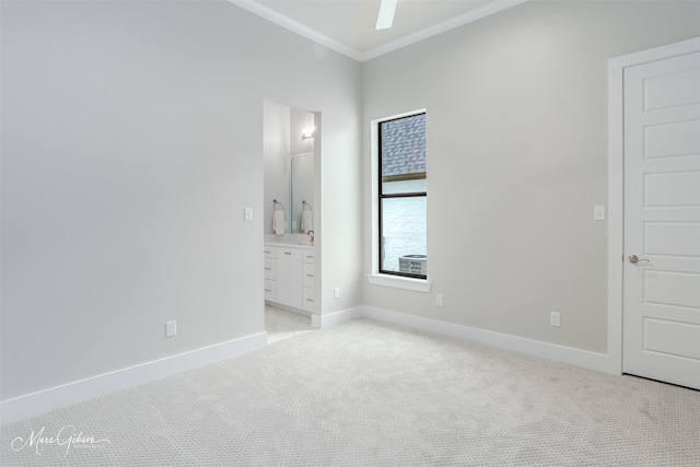 unfurnished bedroom featuring light colored carpet, ensuite bathroom, crown molding, and baseboards