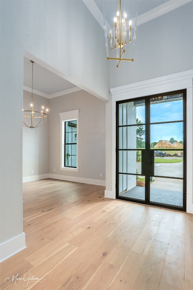 interior space with ornamental molding, a towering ceiling, a chandelier, and light hardwood / wood-style floors