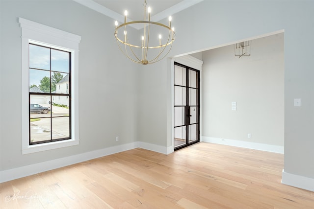 empty room featuring crown molding, plenty of natural light, light hardwood / wood-style floors, and an inviting chandelier