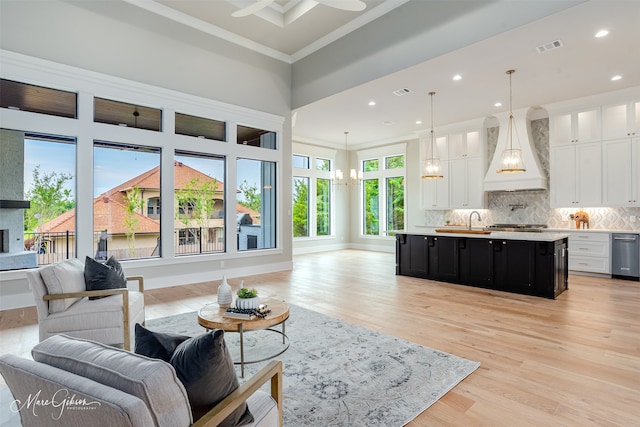 living room with sink, a large fireplace, an inviting chandelier, crown molding, and light hardwood / wood-style floors