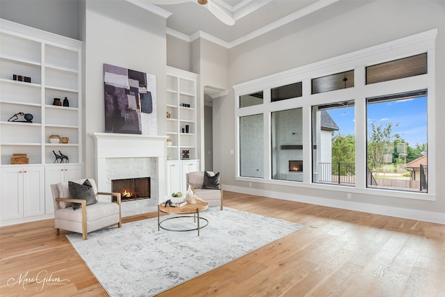 living area with a high end fireplace, crown molding, baseboards, light wood-style flooring, and a towering ceiling