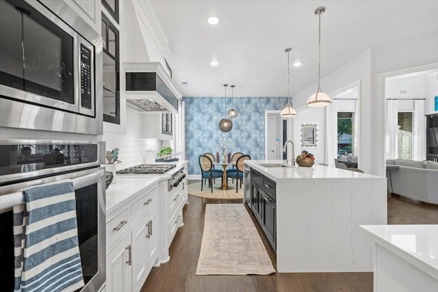 kitchen with white cabinets, sink, an island with sink, appliances with stainless steel finishes, and decorative light fixtures