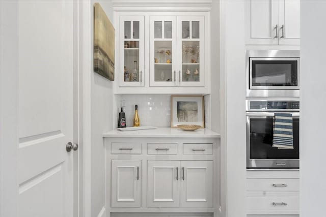 interior space featuring backsplash, stainless steel appliances, and white cabinetry