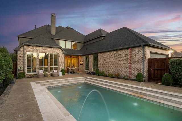 back house at dusk with pool water feature and a patio