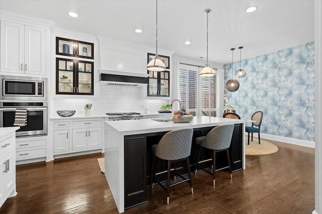 kitchen featuring a center island with sink, hanging light fixtures, a kitchen bar, white cabinetry, and stainless steel appliances