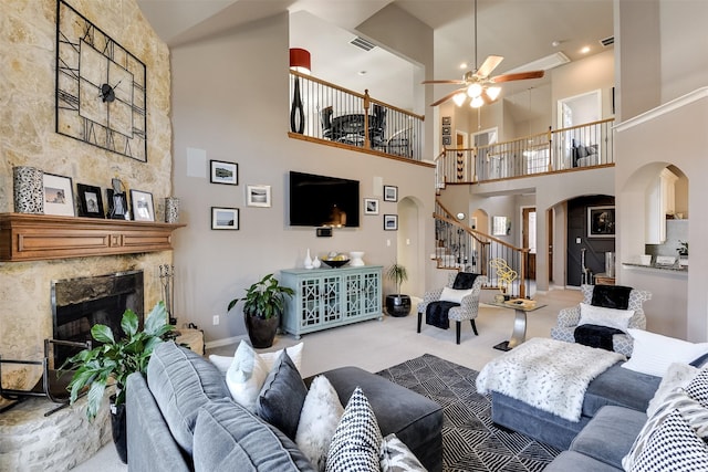 living room featuring ceiling fan, a stone fireplace, carpet floors, and a high ceiling