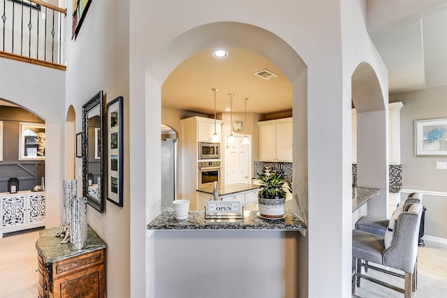 kitchen with appliances with stainless steel finishes, tasteful backsplash, pendant lighting, dark stone countertops, and white cabinetry