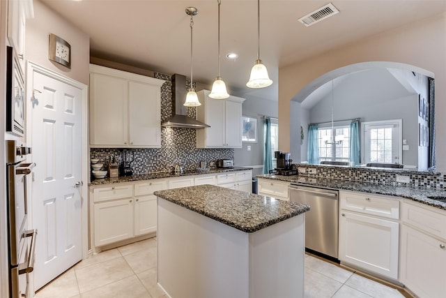 kitchen featuring a center island, white cabinets, wall chimney range hood, appliances with stainless steel finishes, and decorative light fixtures