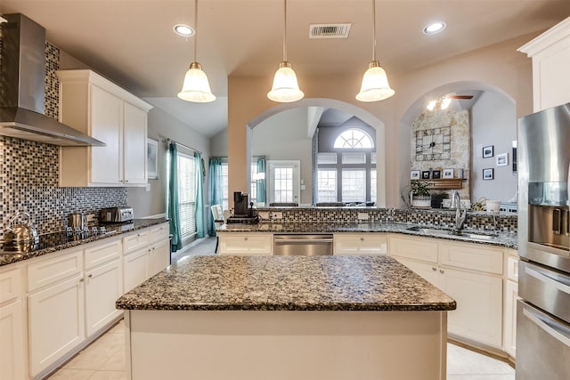 kitchen featuring appliances with stainless steel finishes, sink, wall chimney range hood, pendant lighting, and a kitchen island