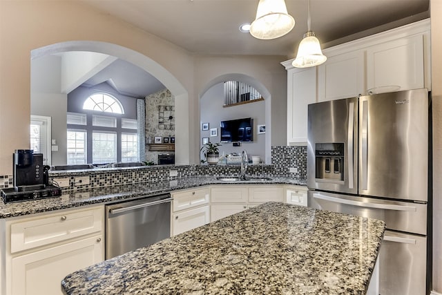 kitchen with stainless steel appliances, white cabinetry, dark stone counters, and sink