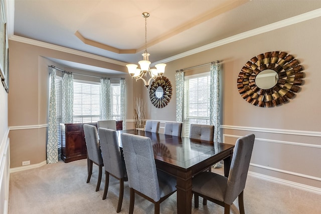 dining room with light carpet, a tray ceiling, an inviting chandelier, and ornamental molding