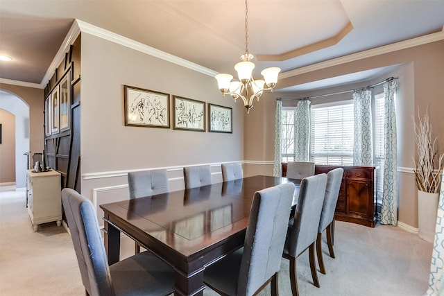 carpeted dining area with an inviting chandelier, ornamental molding, and a tray ceiling