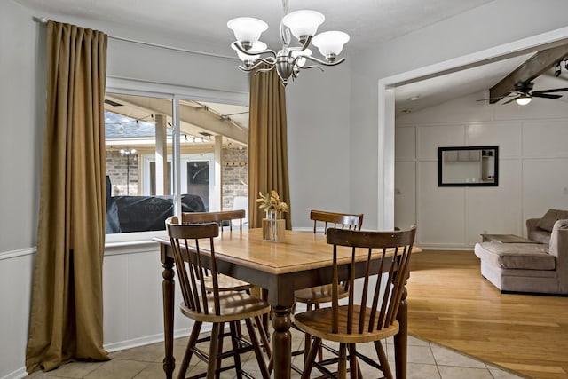 tiled dining space featuring ceiling fan with notable chandelier and vaulted ceiling