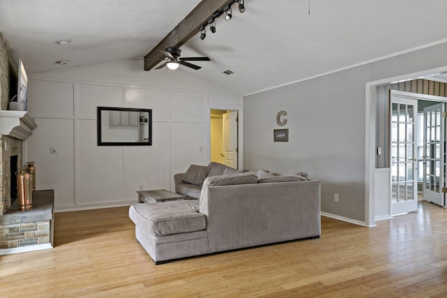 living room with light wood-type flooring, track lighting, ceiling fan, a fireplace, and vaulted ceiling with beams