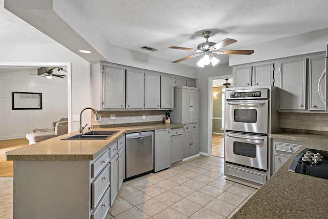 kitchen featuring kitchen peninsula, appliances with stainless steel finishes, tasteful backsplash, gray cabinetry, and sink