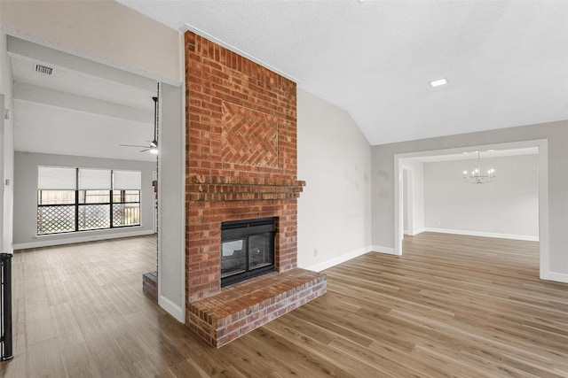 unfurnished living room with hardwood / wood-style floors, ceiling fan with notable chandelier, a brick fireplace, vaulted ceiling, and a textured ceiling