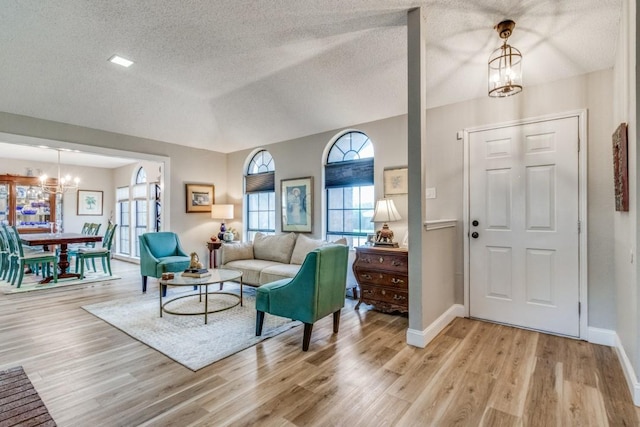 living room featuring lofted ceiling, light wood-type flooring, a textured ceiling, and an inviting chandelier