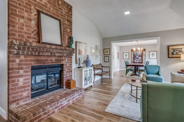 living room with a textured ceiling, vaulted ceiling, a chandelier, a fireplace, and light hardwood / wood-style floors