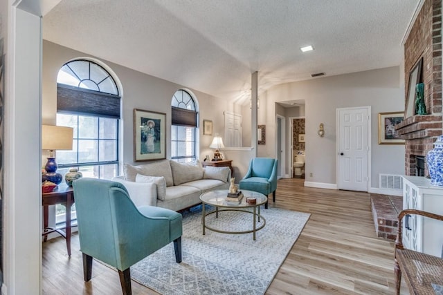 living room featuring a brick fireplace, light wood-type flooring, a textured ceiling, and vaulted ceiling