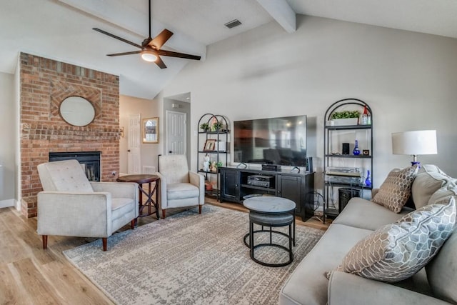 living room with a fireplace, ceiling fan, high vaulted ceiling, light hardwood / wood-style flooring, and beamed ceiling