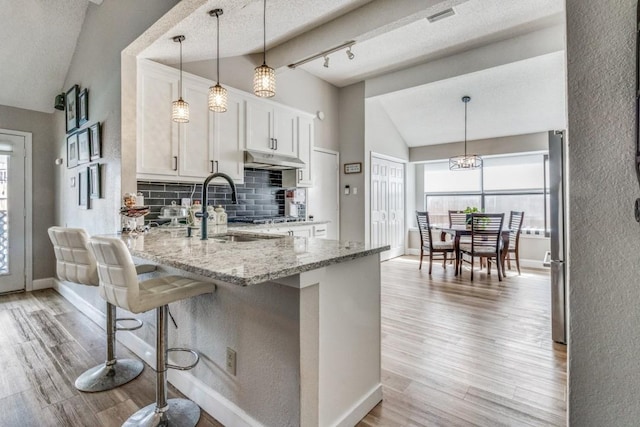 kitchen with light stone countertops, backsplash, white cabinetry, and lofted ceiling