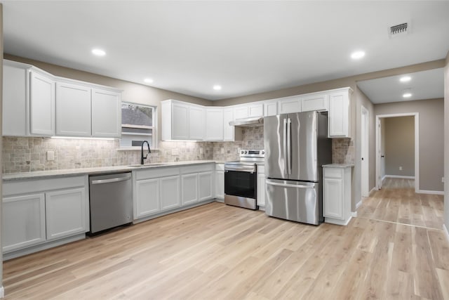 kitchen with white cabinets, sink, light wood-type flooring, appliances with stainless steel finishes, and light stone counters