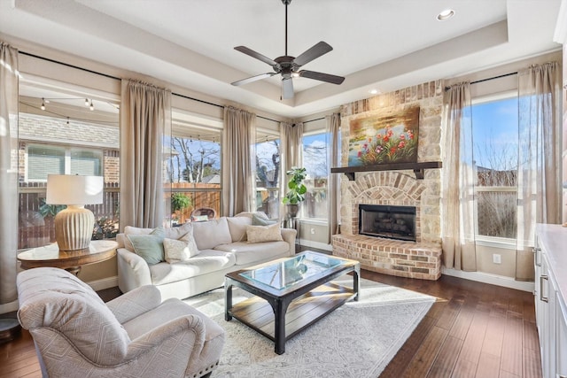 living room featuring a tray ceiling, a healthy amount of sunlight, a fireplace, and dark wood-type flooring