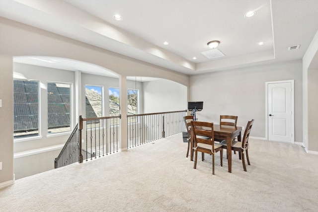 dining space with a tray ceiling and light colored carpet