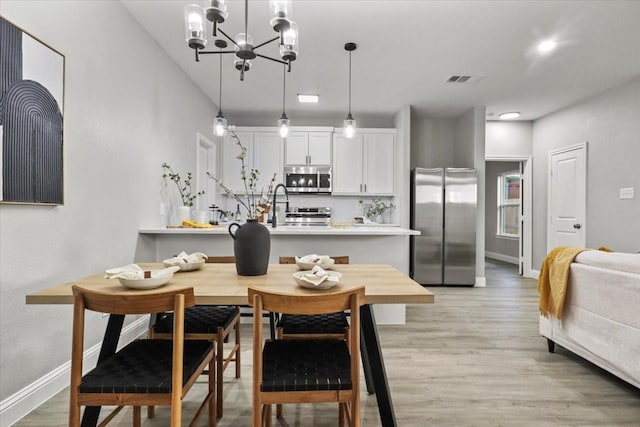 dining space with light wood-type flooring, an inviting chandelier, and sink