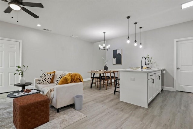 kitchen with ceiling fan with notable chandelier, sink, white cabinets, hanging light fixtures, and a breakfast bar area