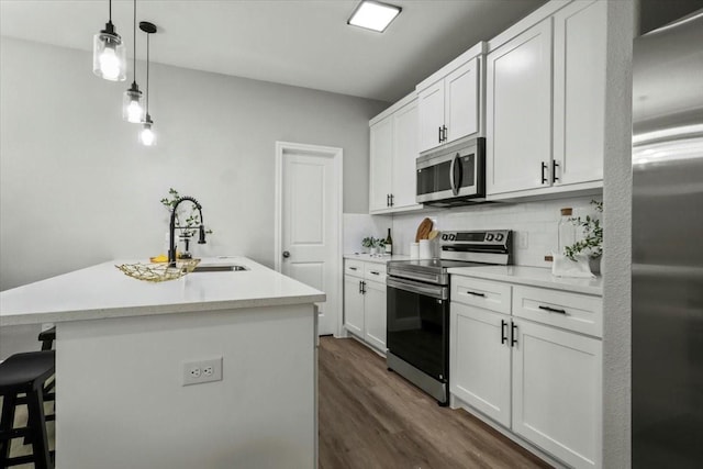 kitchen with white cabinetry, sink, stainless steel appliances, tasteful backsplash, and a center island with sink