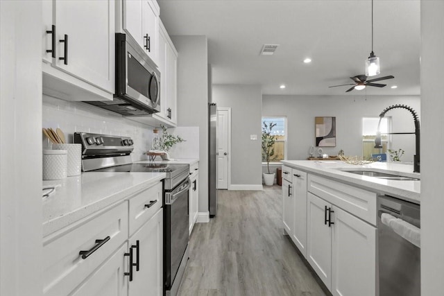 kitchen with appliances with stainless steel finishes, ceiling fan, sink, light hardwood / wood-style flooring, and white cabinetry