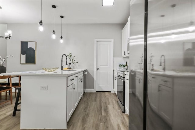 kitchen with a breakfast bar, sink, hanging light fixtures, light hardwood / wood-style floors, and white cabinetry