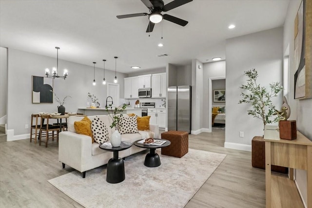 living room with ceiling fan with notable chandelier, sink, and light hardwood / wood-style flooring