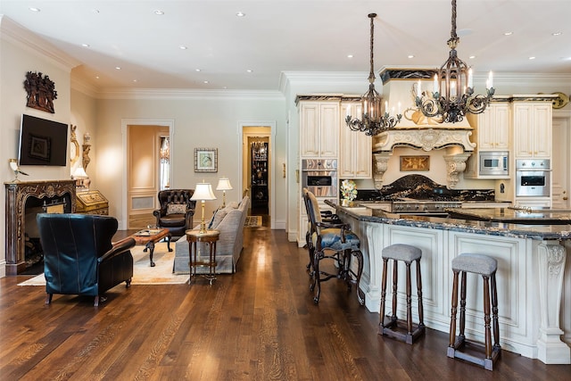 kitchen with dark stone counters, a breakfast bar, decorative light fixtures, cream cabinetry, and stainless steel microwave