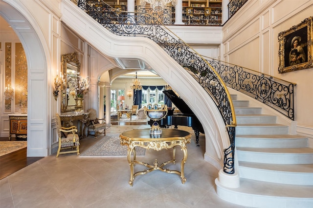 stairway with tile patterned flooring, a notable chandelier, decorative columns, a towering ceiling, and ornamental molding