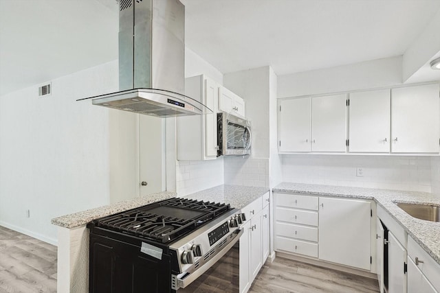 kitchen with white cabinets, light stone countertops, wall chimney range hood, and appliances with stainless steel finishes