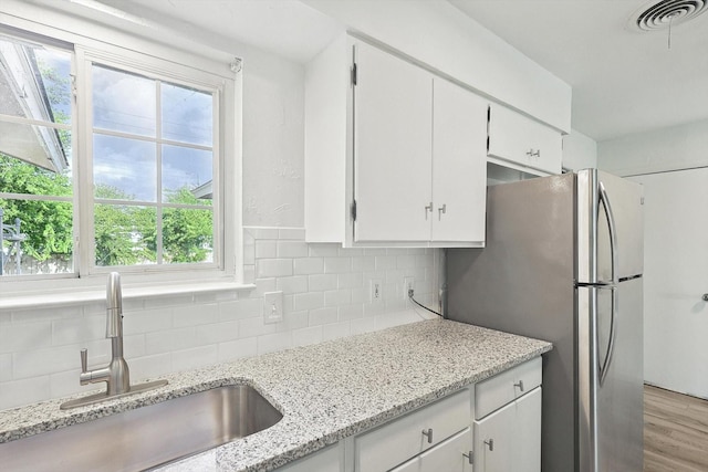 kitchen featuring white cabinets, light stone counters, stainless steel refrigerator, and sink